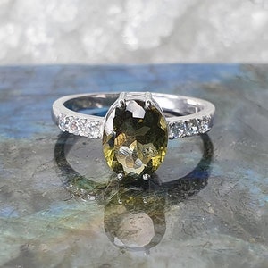 May include: A silver ring with a large oval-shaped green gemstone surrounded by smaller clear gemstones.