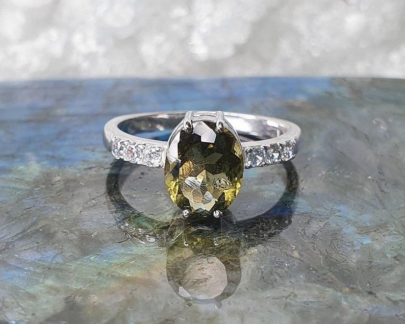 May include: A silver ring with a large oval-shaped green gemstone surrounded by smaller clear gemstones.