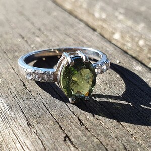 May include: A silver ring with a green oval gemstone and a band of small clear stones.