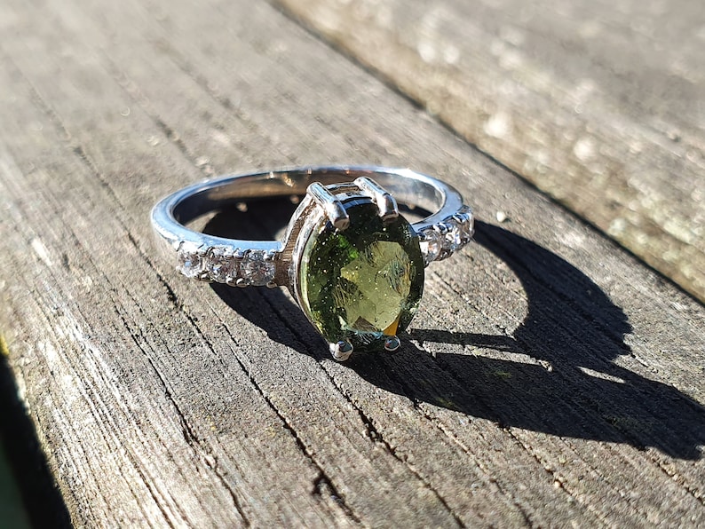 May include: A silver ring with a green oval gemstone and a band of small clear stones.