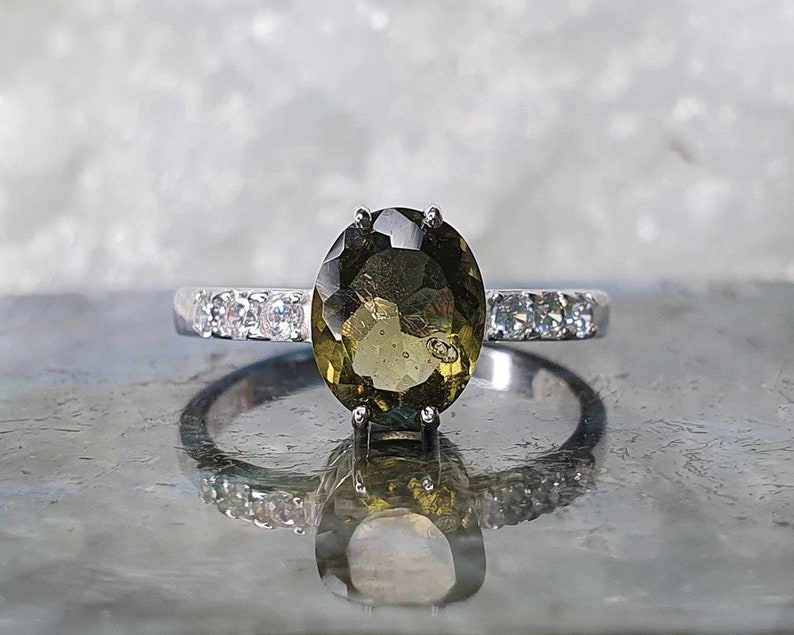 May include: A silver ring with a large oval-shaped green gemstone surrounded by smaller clear gemstones.