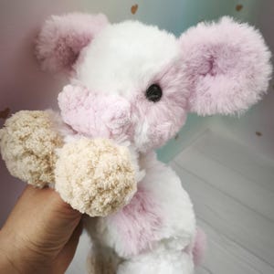 Pode incluir: Um coelho de pel&uacute;cia com corpo branco, detalhes rosa e patas bege. O coelho tem orelhas grandes e fofas rosa e uma express&atilde;o doce. O brinquedo &eacute; macio e aconchegante, para o conforto de uma crian&ccedil;a.