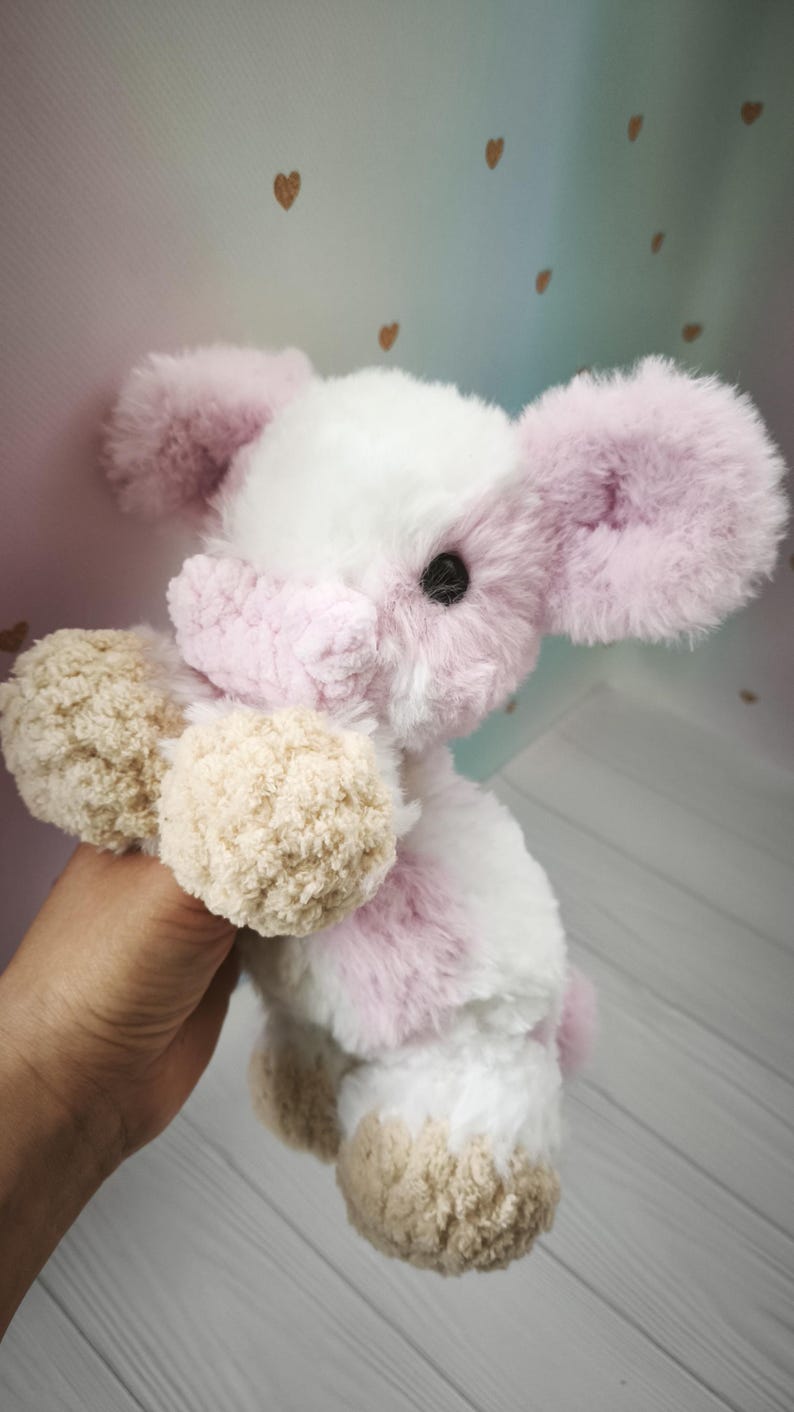 Pode incluir: Um coelho de pel&uacute;cia com corpo branco, detalhes rosa e patas bege. O coelho tem orelhas grandes e fofas rosa e uma express&atilde;o doce. O brinquedo &eacute; macio e aconchegante, para o conforto de uma crian&ccedil;a.