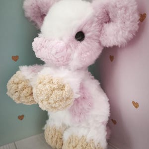 Pode incluir: Um elefante de pel&uacute;cia em tons de rosa, branco e bege. O elefante tem orelhas grandes e fofas, uma cabe&ccedil;a branca e detalhes em rosa no corpo. Seus p&eacute;s s&atilde;o bege e tem um olho de bot&atilde;o preto.