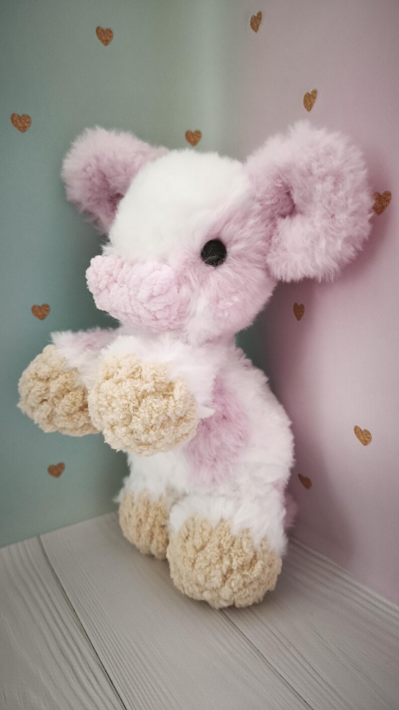 Pode incluir: Um elefante de pel&uacute;cia em tons de rosa, branco e bege. O elefante tem orelhas grandes e fofas, uma cabe&ccedil;a branca e detalhes em rosa no corpo. Seus p&eacute;s s&atilde;o bege e tem um olho de bot&atilde;o preto.