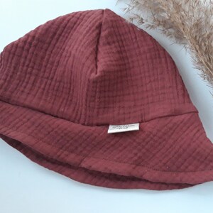 May include: A maroon-colored bucket hat made of soft, textured fabric. The hat has a wide brim and a small label sewn on the front that says "Organic Cotton".