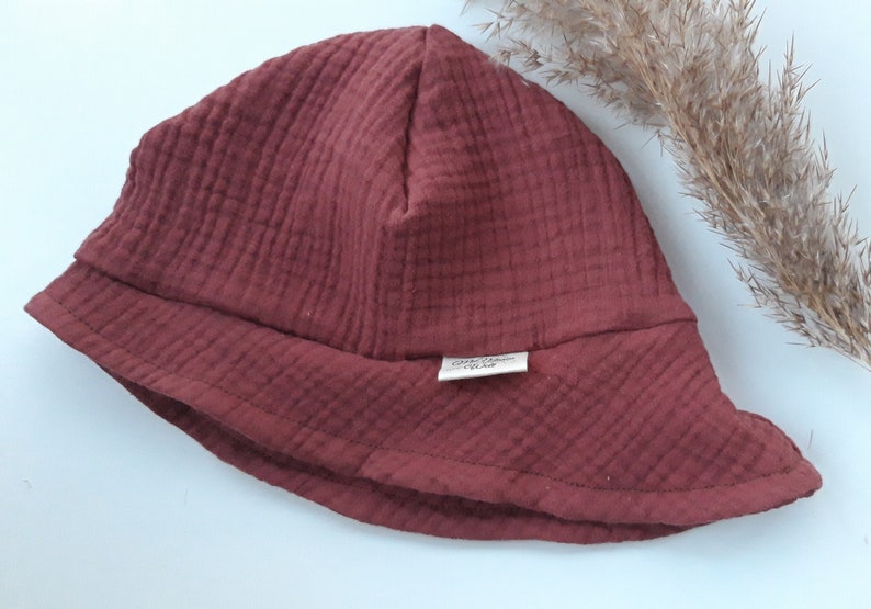 May include: A maroon-colored bucket hat made of soft, textured fabric. The hat has a wide brim and a small label sewn on the front that says "Organic Cotton".