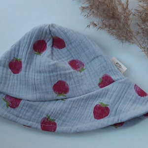 May include: A gray cotton sun hat with a strawberry print. The hat has a wide brim and a small label that says "Baby"