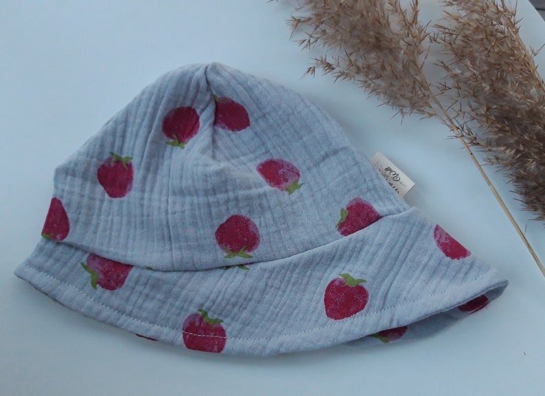 May include: A gray cotton sun hat with a strawberry print. The hat has a wide brim and a small label that says "Baby"