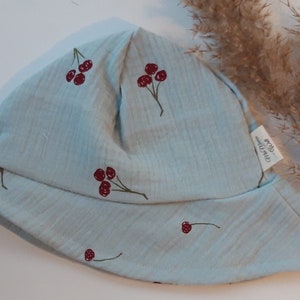 May include: A light blue sun hat with a cherry print. The hat has a small label that says "One Hundred Percent Organic Cotton".