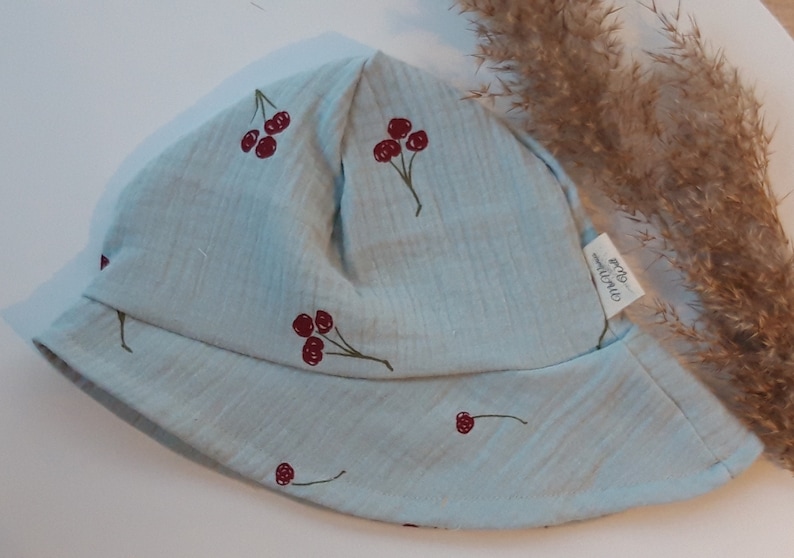 May include: A light blue sun hat with a cherry print. The hat has a small label that says "One Hundred Percent Organic Cotton".