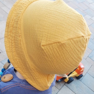May include: A yellow sun hat with a wide brim and a textured fabric. The hat is made of a soft, breathable material and is perfect for protecting your child's face from the sun.