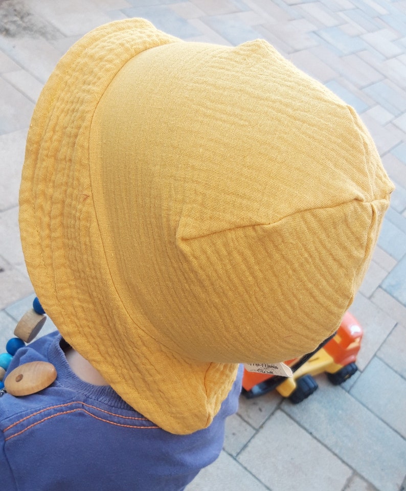 May include: A yellow sun hat with a wide brim and a textured fabric. The hat is made of a soft, breathable material and is perfect for protecting your child's face from the sun.