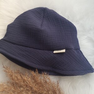 May include: A dark blue, wide-brimmed bucket hat made of soft, textured fabric. The hat has a small, white label with the text "simple life" on it.