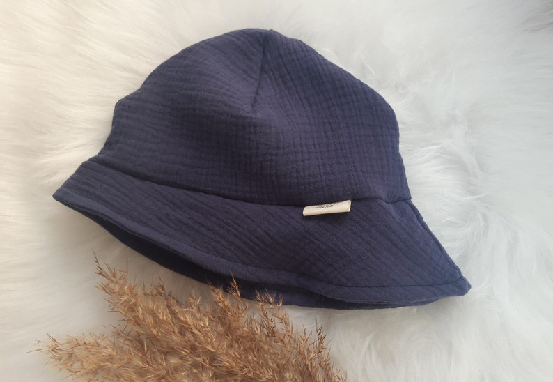 May include: A dark blue, wide-brimmed bucket hat made of soft, textured fabric. The hat has a small, white label with the text "simple life" on it.