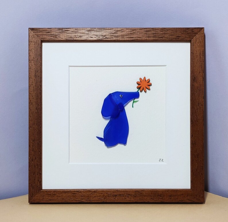 May include: A framed artwork featuring a blue glass dog sniffing an orange flower. The artwork is signed "ER".