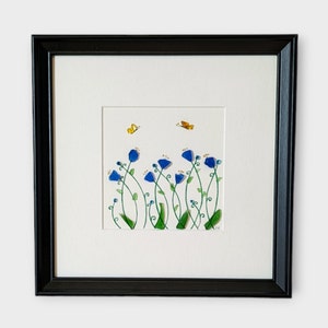 May include: A framed artwork featuring a watercolor painting of blue flowers with green stems and leaves. Two yellow butterflies are flying above the flowers.