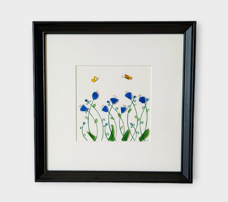 May include: A framed artwork featuring a watercolor painting of blue flowers with green stems and leaves. Two yellow butterflies are flying above the flowers.