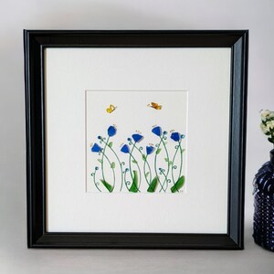 May include: A framed artwork featuring a watercolor painting of blue flowers with green stems and yellow butterflies on a white background.