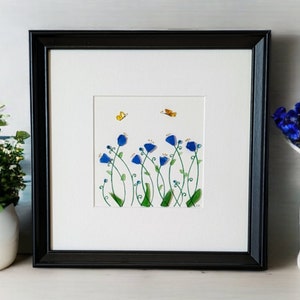 May include: Framed artwork featuring a blue flower arrangement with green stems and yellow butterflies on a white background.
