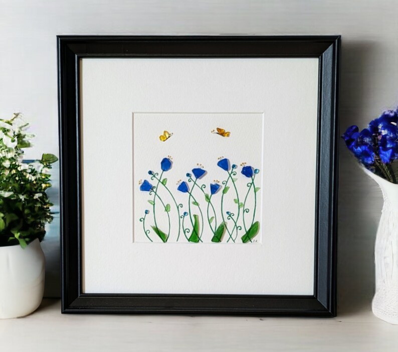May include: Framed artwork featuring a blue flower arrangement with green stems and yellow butterflies on a white background.