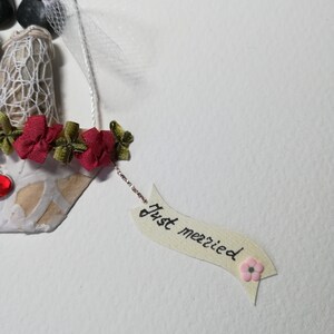 May include: A handmade wedding card with a couple made of stones, a white veil, and red flowers. The card has a banner that says "Just married" with a pink flower.
