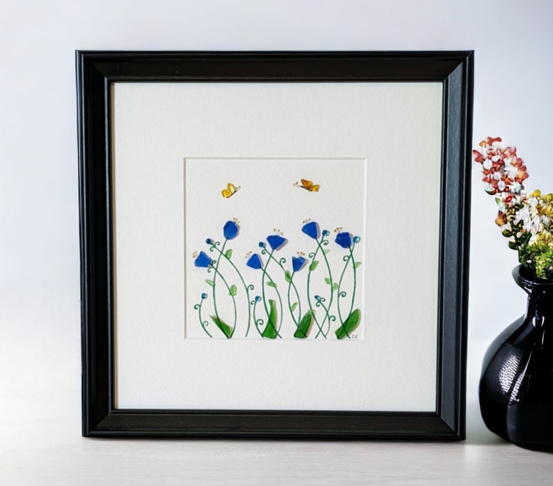 May include: Framed artwork featuring a watercolor painting of blue flowers with green stems and two yellow butterflies against a white background.