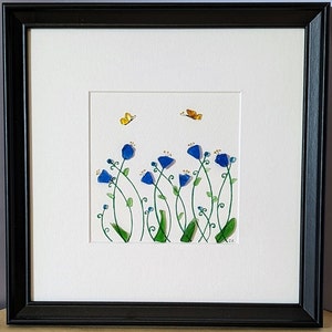 May include: A framed artwork featuring a blue and green glass mosaic of flowers and butterflies on a white background. The artwork is signed "SK" in the bottom right corner.