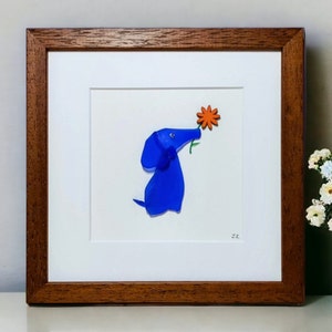 May include: A framed artwork featuring a blue glass dog sniffing an orange flower. The artwork is signed '22' in the bottom right corner.