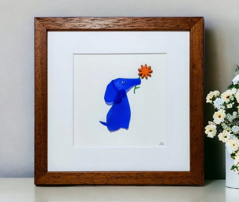 May include: A framed artwork featuring a blue glass dog sniffing an orange flower. The artwork is signed '22' in the bottom right corner.