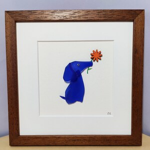 May include: A framed artwork featuring a blue glass dog sniffing a red flower. The artwork is on a white background and has a brown frame.
