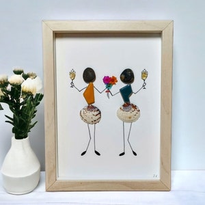Può includere: Un'opera d'arte incorniciata con due figure realizzate con pietre e conchiglie. Le figure sono vestite con abiti colorati e tengono un bicchiere di champagne e un mazzo di fiori. L'opera è firmata "ZV".