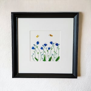 May include: Framed artwork featuring a blue flower arrangement with green stems and yellow butterflies on a white background.