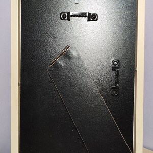 Op de afbeelding: Een licht houten fotolijst met een zwarte achterkant en een zwarte ezelstandaard. De lijst heeft twee metalen ophanghaken aan de achterkant.