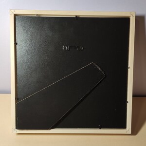 May include: A white picture frame with a black mat and a black easel stand on the back.