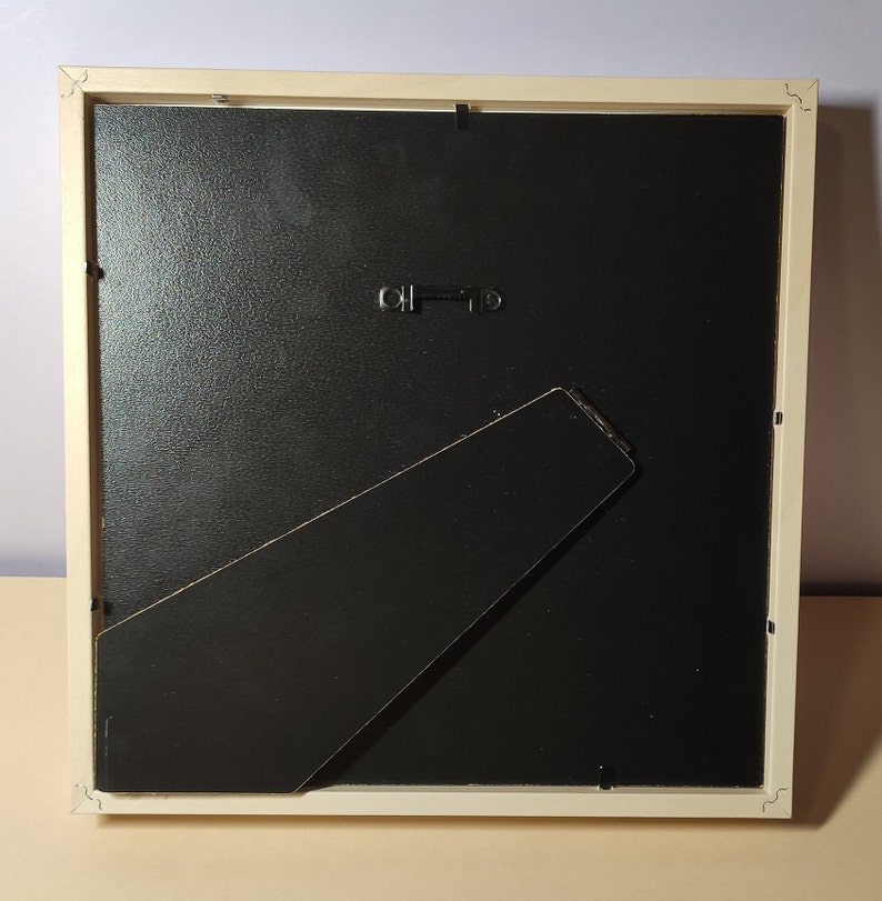 May include: A white picture frame with a black mat and a black easel stand on the back.
