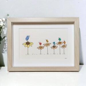 Op de afbeelding: Een ingelijst kunstwerk met een rij kleurrijke vogels die op gele bloemen zitten. De vogels zijn gemaakt van beschilderde stenen en de bloemen van beschilderde kiezelsteentjes. Het kunstwerk is gesigneerd met "JC".