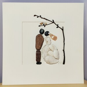 May include: A framed artwork made with stones and shells depicting a bride and groom standing under a branch with two birds perched on it. The artwork is signed "J.K."