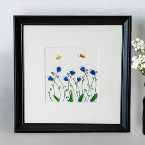 May include: Framed artwork featuring a watercolor painting of blue flowers with green stems and yellow butterflies on a white background.