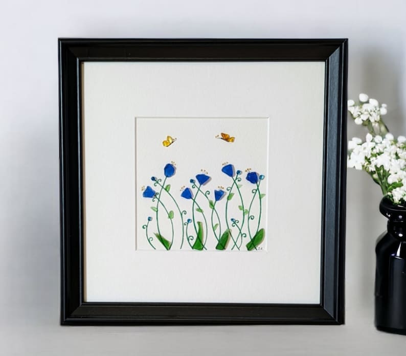 May include: Framed artwork featuring a watercolor painting of blue flowers with green stems and yellow butterflies on a white background.