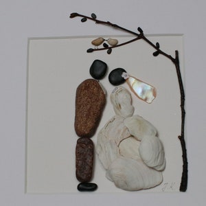 May include: A framed artwork made with stones and shells depicting a bride and groom standing under a branch with two birds perched on it. The bride is wearing a white dress made of shells and the groom is wearing a brown suit made of stones. The artwork is signed "D.K."
