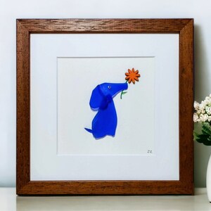 May include: A framed artwork featuring a blue glass dog sniffing a bright orange flower. The artwork is signed with the initials "M.K."