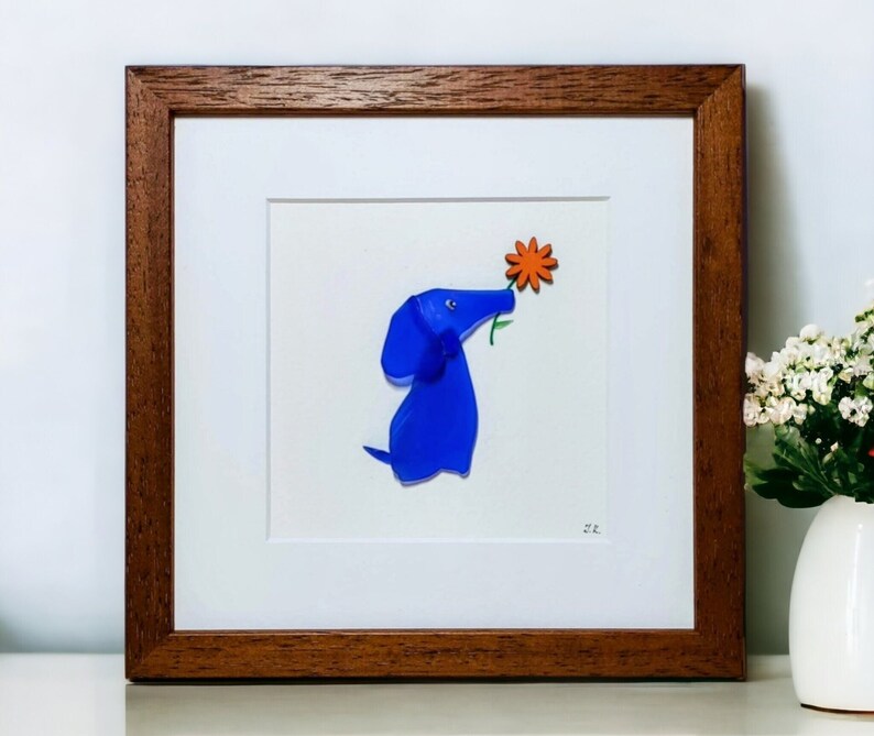 May include: A framed artwork featuring a blue glass dog sniffing a bright orange flower. The artwork is signed with the initials "M.K."