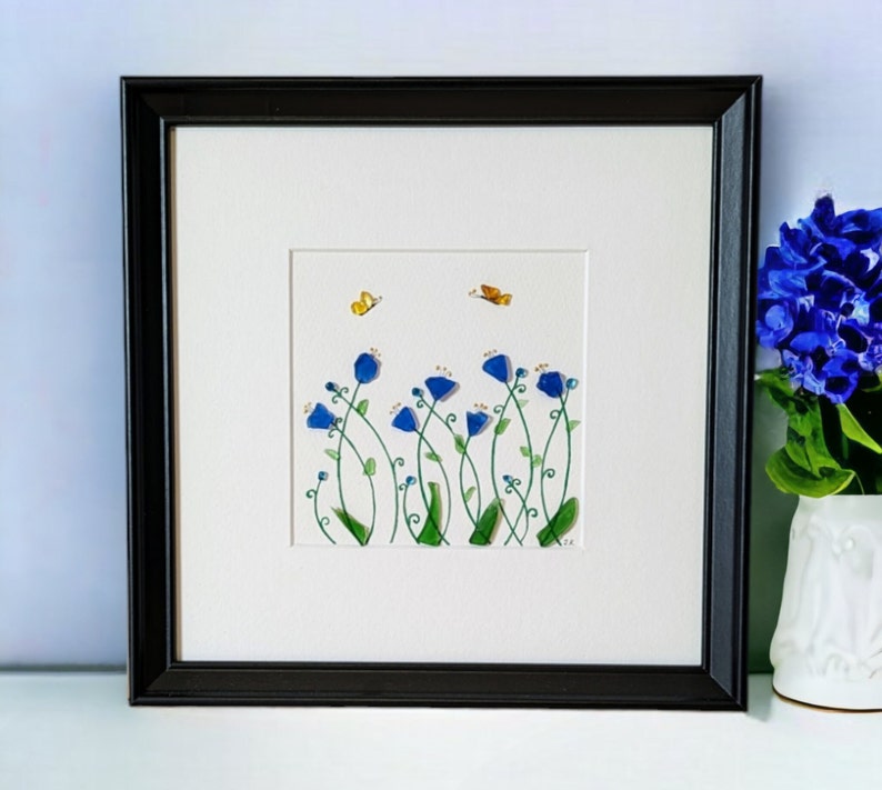 May include: Framed artwork featuring a watercolor painting of blue flowers with green stems and yellow butterflies on a white background.