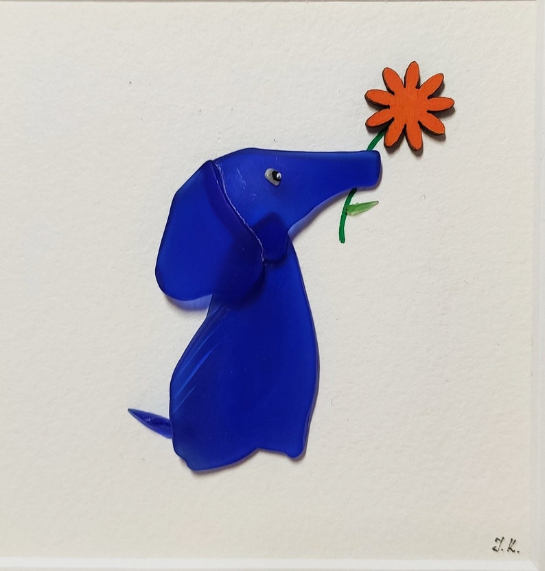 May include: A blue glass dachshund figurine holding a red flower. The figurine is on a white background with the artist's signature in the bottom right corner.