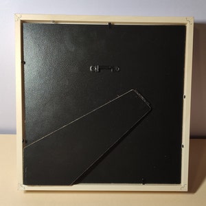 May include: A white picture frame with a black mat and a black easel stand on the back. The frame is made of wood and has a simple design.