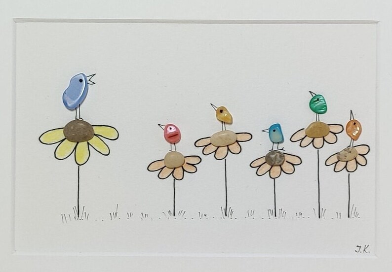 Op de afbeelding: Een kleurrijk beeld van kiezelkunst met zes vogels die op gele bloemen met groene stelen zitten. De vogels zijn blauw, geel, groen, roze en oranje. De achtergrond is wit met de initialen van de kunstenaar "J.K." in de rechterbenedenhoek.