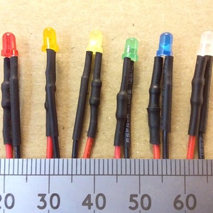May include: Six LED lights with different coloured lenses, red, yellow, yellow, green, blue, and white, are wired with black and red wires and heat shrink tubing. The lights are measured on a ruler with markings from 0 to 70.