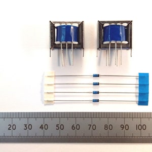 May include: Two blue and silver electrical transformers and a set of four diodes with a ruler for scale. The transformers have blue cylindrical components. The diodes are connected by silver wires and have blue and white plastic ends.