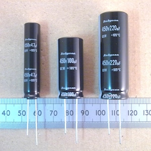 May include: Three black cylindrical Rubycon capacitors with white text, labeled with voltage and capacitance values. The capacitors are arranged in a row, with a ruler in the foreground. The capacitors have three wire leads.